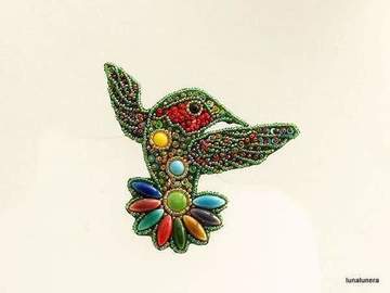 Colección Broches de Porcelana. Broche con forma de colibrí hecho con pedrería y piezas de porcelana, de color verde y cola multicolor.