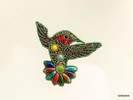 Colección Broches de Porcelana. Broche con forma de colibrí hecho con pedrería y piezas de porcelana, de color verde y cola multicolor.